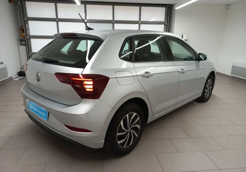 Volkswagen Polo 2024 couleur reflet d'argent vue 3/4 arrière droit avec feux arrière allumés en intérieur showroom.