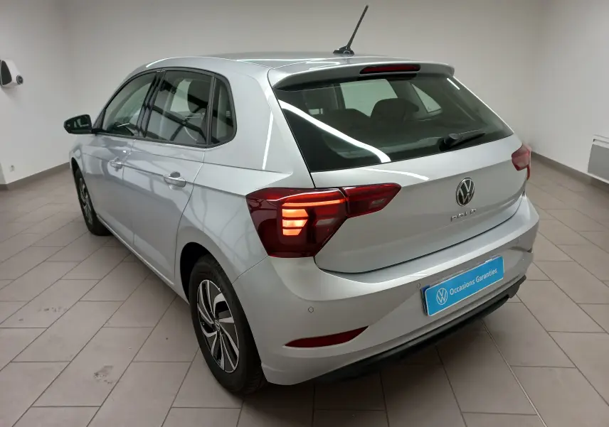 Vue 3/4 arrière droite d'une Volkswagen Polo 2024 argent avec feux allumés et caméra de recul visible sur le pare-chocs.