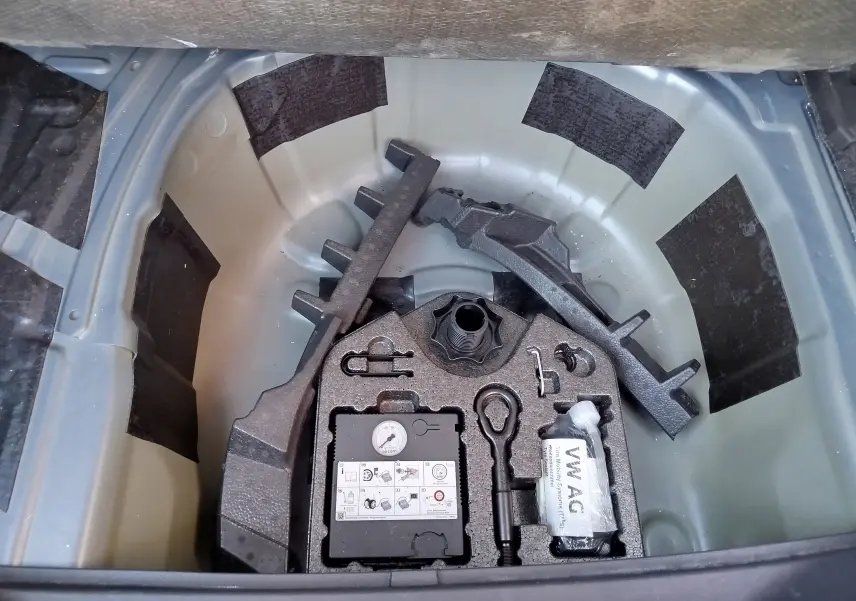 Vue plongeante sur le coffre ouvert d'une SEAT Arona bleu électrique, montrant le rangement des outils et compresseur.