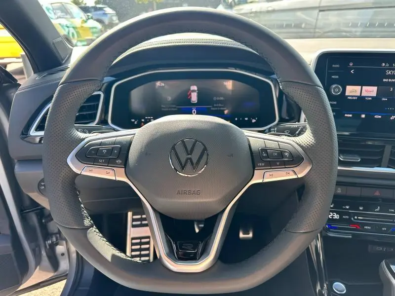 Vue rapprochée du volant cuir multifonction gris du Volkswagen T-Roc 2025 avec tableau de bord numérique et écran tactile.