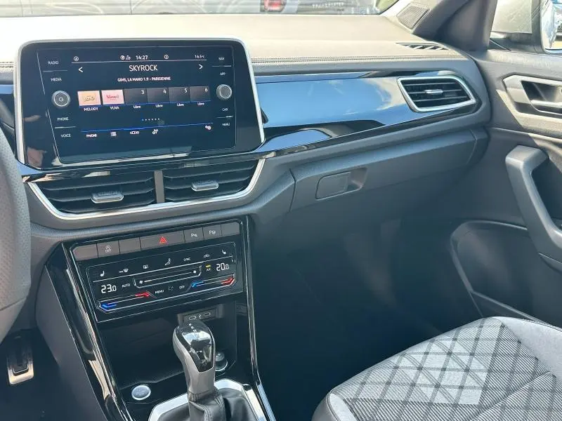 Intérieur avant droit du Volkswagen T-Roc 2025 avec tableau de bord noir brillant et écran tactile multimédia allumé.