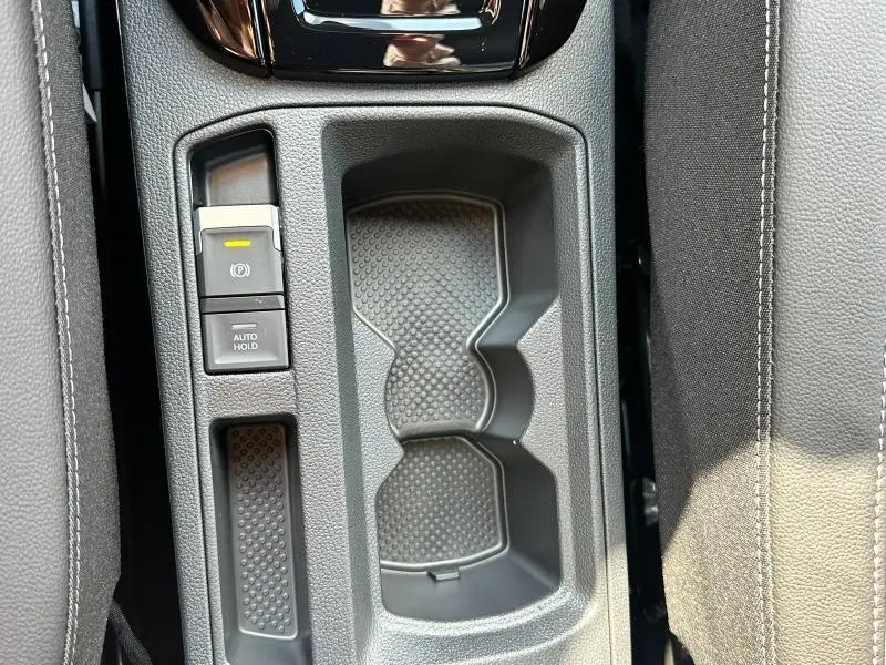 Gros plan sur la console centrale grise du Volkswagen T-Roc 2025 avec porte-gobelets et commandes frein à main électrique.