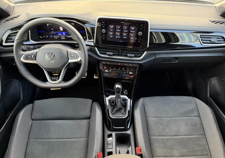 Vue intérieure du tableau de bord et console centrale du Volkswagen T-Roc 2025 avec volant multifonction et écran tactile.