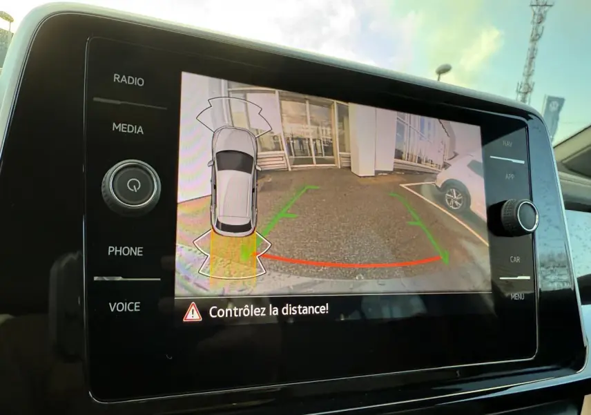 Écran de caméra de recul affichant l'arrière d'un Volkswagen T-Roc bleu pétrole en stationnement, vue intérieure console centrale.