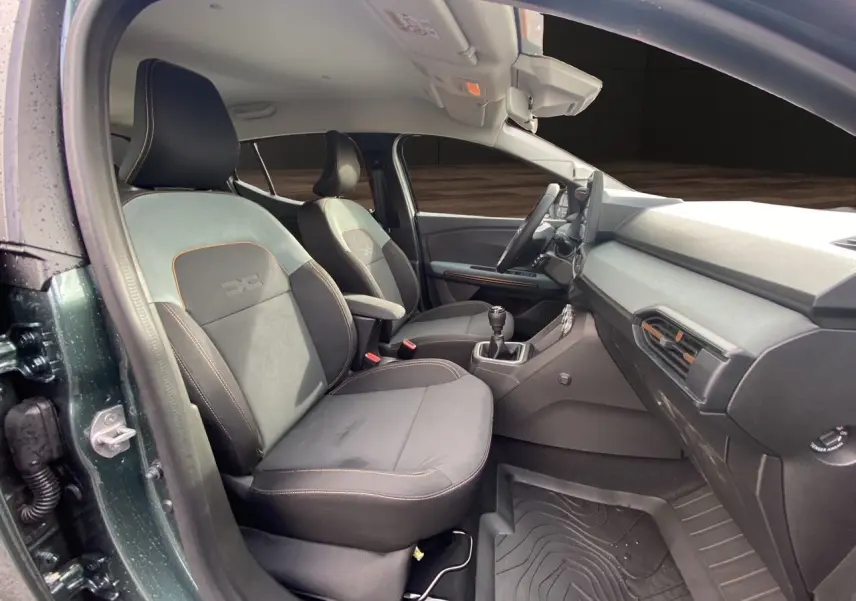 Vue intérieure côté conducteur du Dacia Sandero Stepway 2026 vert cèdre, sièges tissu gris noir avec surpiqûres orange.