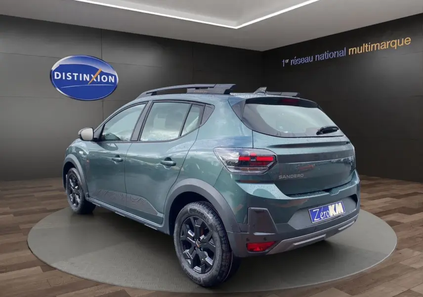 Vue 3/4 arrière droite d’une Dacia Sandero Stepway 2026 vert cèdre métallisé avec jantes alliage noires et barres de toit.