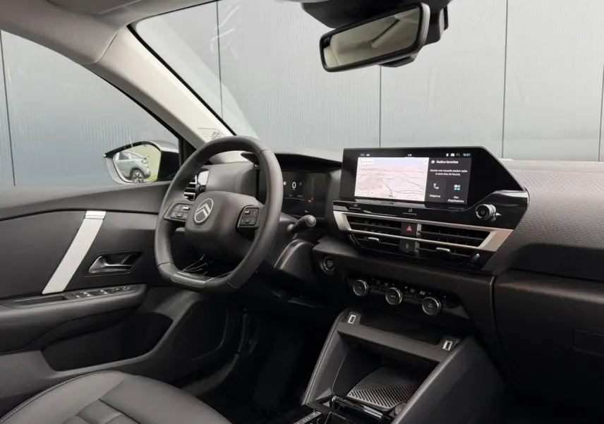 Vue intérieure côté conducteur de la Citroën C4 2025, tableau de bord noir avec écran tactile et volant cuir.