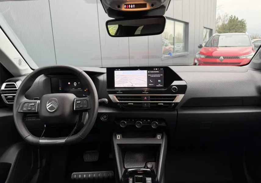 Vue intérieure frontale du tableau de bord noir du Citroën C4 2025 avec écran tactile central et volant multifonctions.