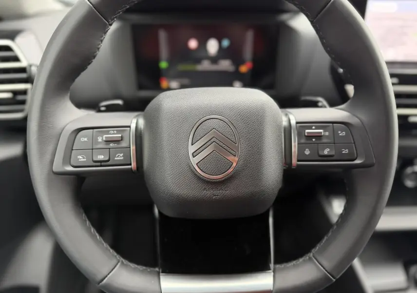 Gros plan sur le volant cuir noir du Citroën C4 2025 avec commandes intégrées et logo chromé au centre.