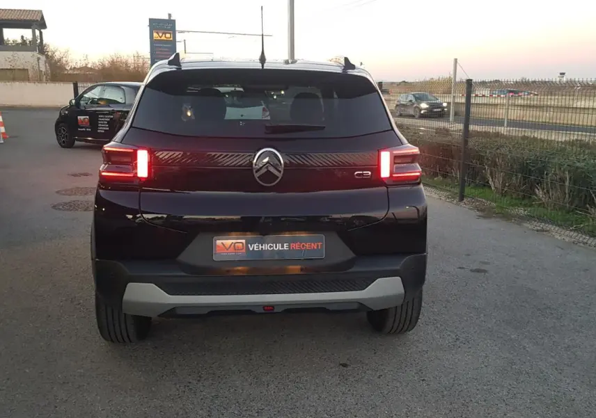 Vue arrière d'une Citroën C3 noire 2025 avec feux allumés et barres de toit visibles en extérieur.