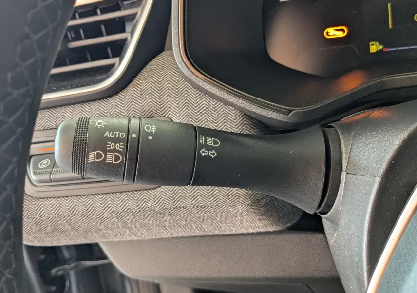 Gros plan sur la commande des feux et clignotants dans l'habitacle gris noir d'une Renault Clio hybride 2025.