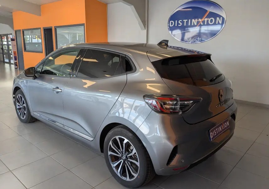 Vue 3/4 arrière droite d'une Renault Clio gris schiste métal 2025 en hybride, stationnée en intérieur avec jantes alliage distinctives.