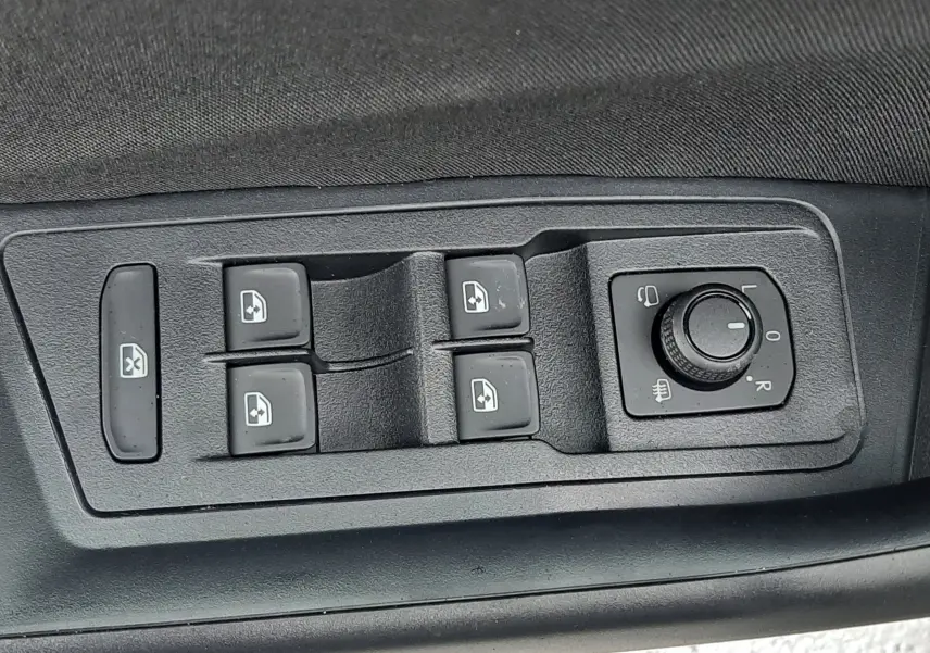 Gros plan sur les commandes de lève-vitres et réglage des rétroviseurs côté gauche du Volkswagen T-Roc gris pyrite 2025.