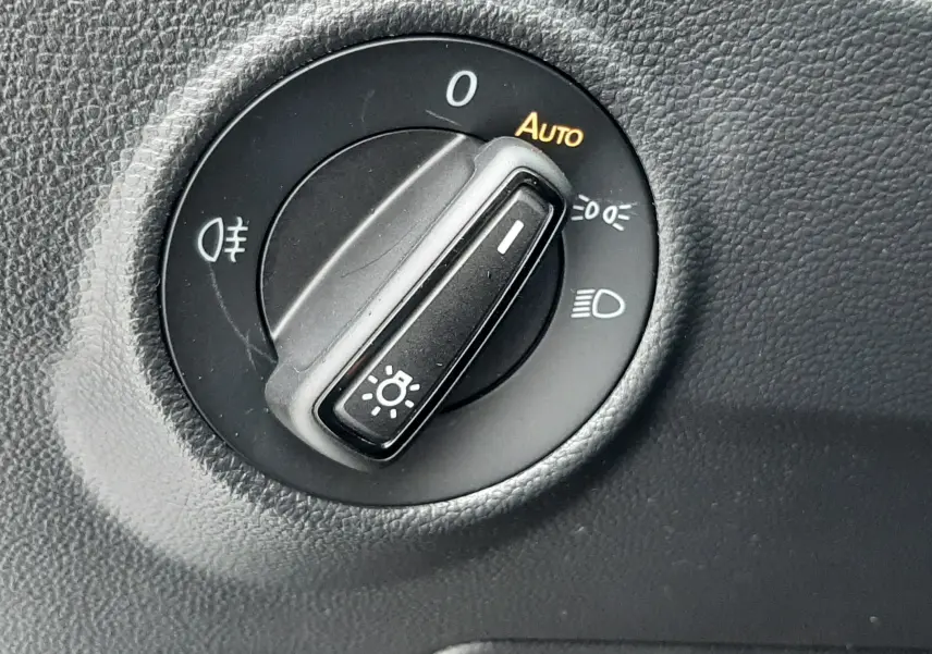 Gros plan sur le sélecteur de phares noir dans l’habitacle du Volkswagen T-Roc gris pyrite 2025.