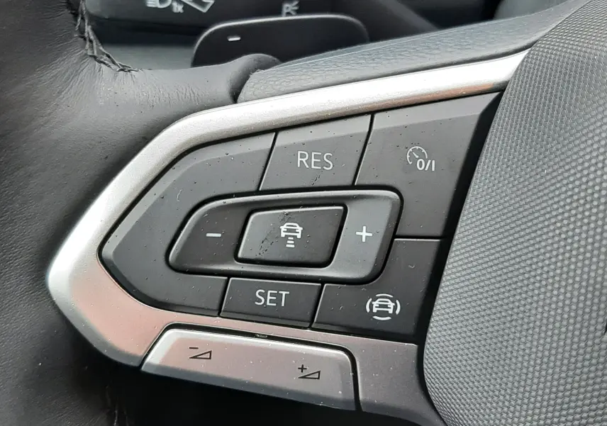 Gros plan sur les commandes au volant côté gauche du Volkswagen T-Roc gris pyrite, mettant en valeur les boutons de régulateur de vitesse.