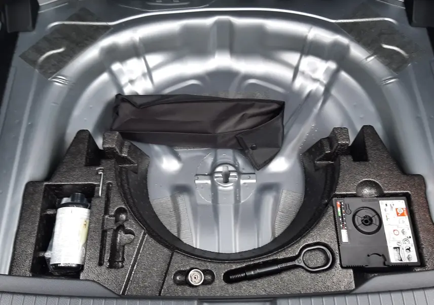 Vue plongeante sur le compartiment de roue de secours gris pyrite d’un Volkswagen T-Roc 2025 avec kit de réparation.