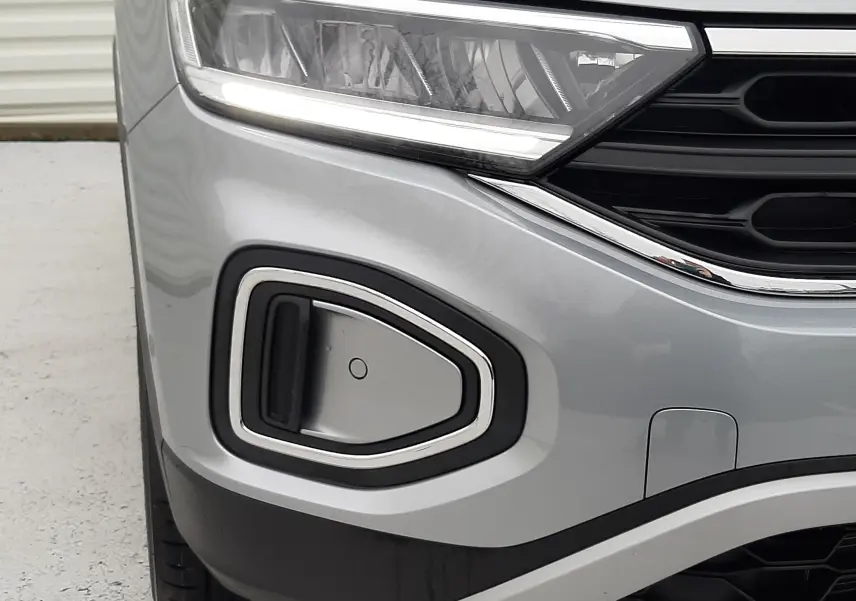 Gros plan sur l'avant gauche du Volkswagen T-Roc gris pyrite, mettant en valeur le phare et la prise d'air chromée.
