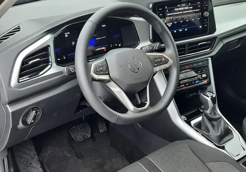 Vue intérieure côté conducteur du Volkswagen T-Roc 2025, tableau de bord noir avec écran tactile et volant multifonction.