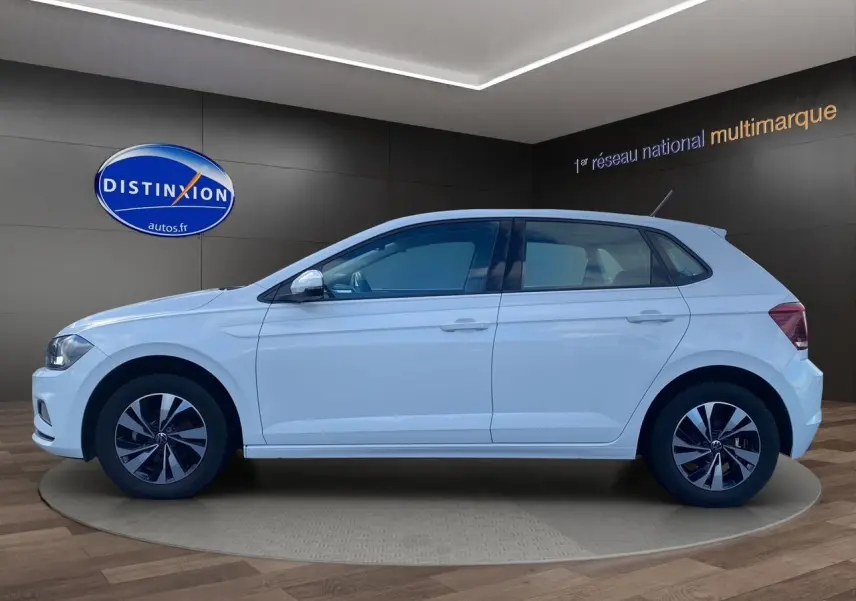 Volkswagen Polo blanc pure vue de profil côté gauche, avec jantes alliage et cinq portes visibles en intérieur showroom.