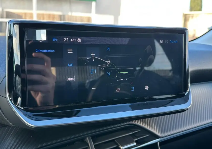 Écran tactile central affichant la climatisation dans l'habitacle d'une Peugeot 208 blanc, vue de face.