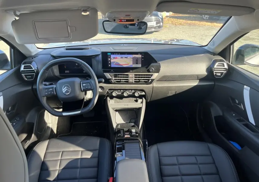 Vue intérieure avant du Citroën C4 X 2025 gris mercure, avec tableau de bord numérique et écran tactile central allumé.
