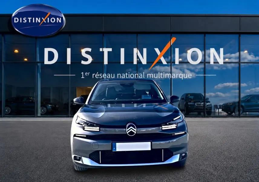 Vue frontale d'une Citroën C4 X gris mercure 2025, avec calandre noire et feux LED distinctifs, devant un showroom Distinxion.