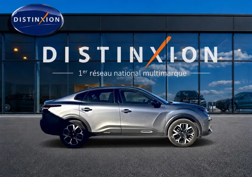 Profil côté gauche d'une Citroën C4 X gris mercure 2025, avec jantes alliage et lignes fluides, devant une vitrine Distinxion.