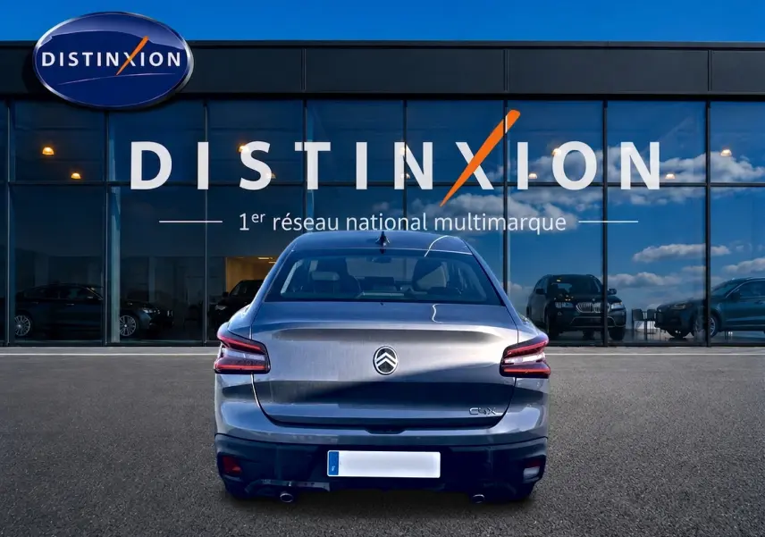 Vue arrière d'une Citroën C4 X gris mercure stationnée devant une vitrine Distinxion avec doubles sorties d'échappement.