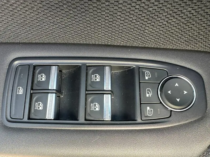 Vue rapprochée des commandes de lève-vitres et rétroviseurs sur la porte intérieure d'une Renault Symbioz rouge.