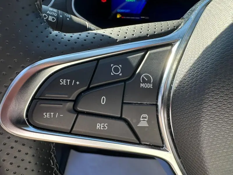 Gros plan sur les commandes multifonctions noires du volant perforé du Renault Symbioz rouge, avec cadre chromé.