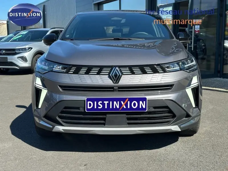 Vue de face d'une Renault Symbioz grise avec calandre chromée et phares LED fins, sur parking extérieur.