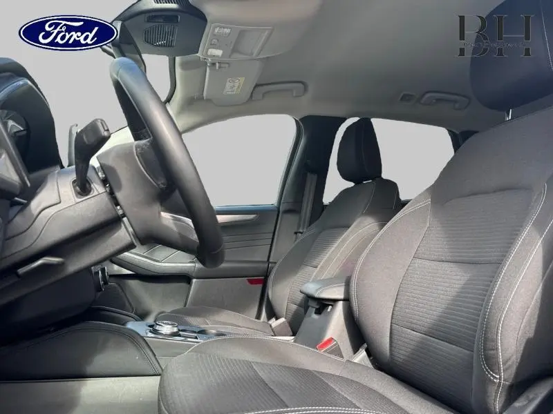Vue intérieure côté conducteur du Ford Kuga 2022, sièges sport tissu noir avec surpiqûres blanches et volant cuir multifonction.