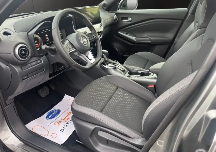 Vue intérieure côté conducteur du Nissan Juke 2025 gris squale, avec sièges et volant chauffants, tableau de bord digital et console centrale.