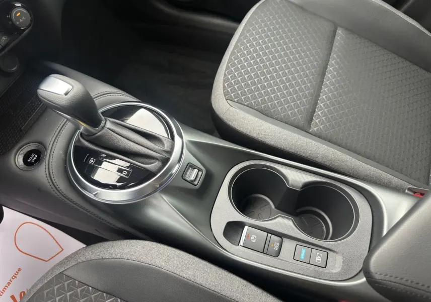 Vue rapprochée de la console centrale du Nissan Juke gris squale 2025, avec levier de boîte auto et sièges tissu gris.