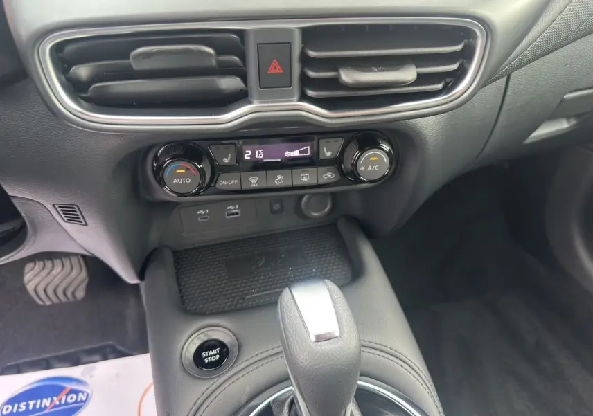 Vue intérieure centrée sur la console centrale du Nissan Juke 2025, montrant la boîte auto et les commandes de climatisation.