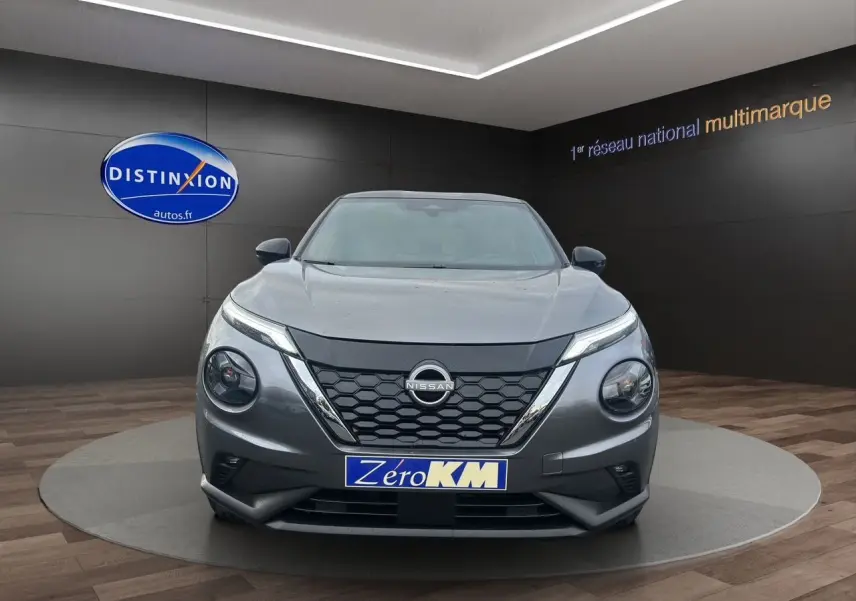 Vue frontale du Nissan Juke 2025 gris squale avec calandre noire et phares ronds distinctifs en showroom.