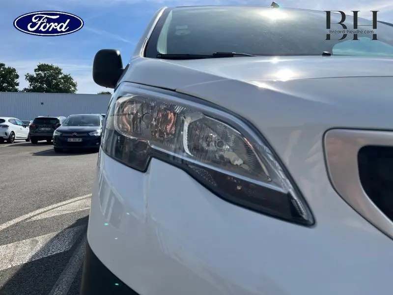 Gros plan sur le phare avant droit du Peugeot Expert Fourgon blanc banquise, avec reflet du soleil sur la carrosserie.