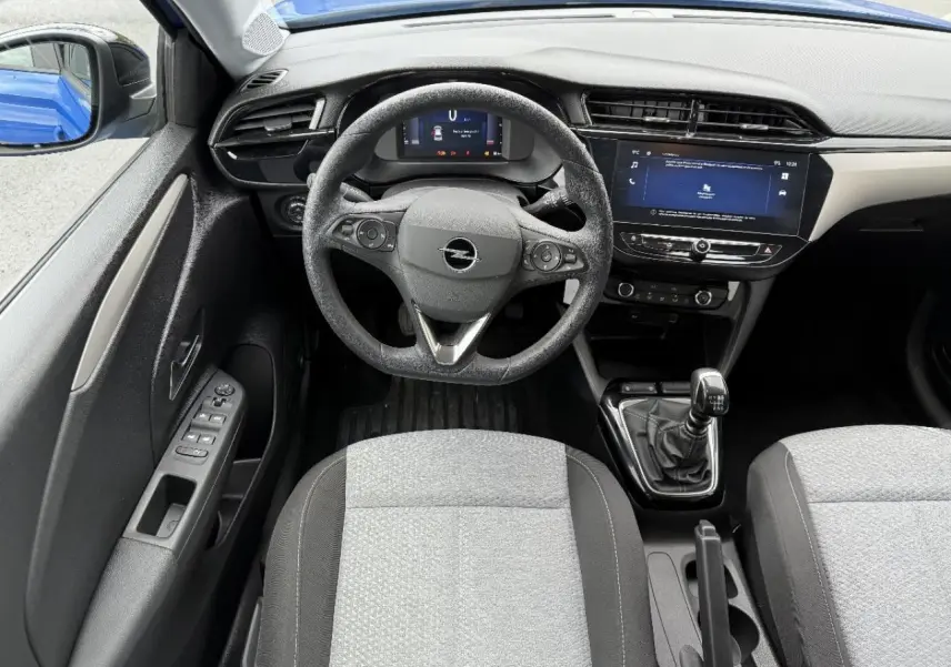 Vue intérieure centrée sur le volant et la console d’une Opel Corsa 2025, boîte manuelle, avec rétroviseur bleu voltaik visible.