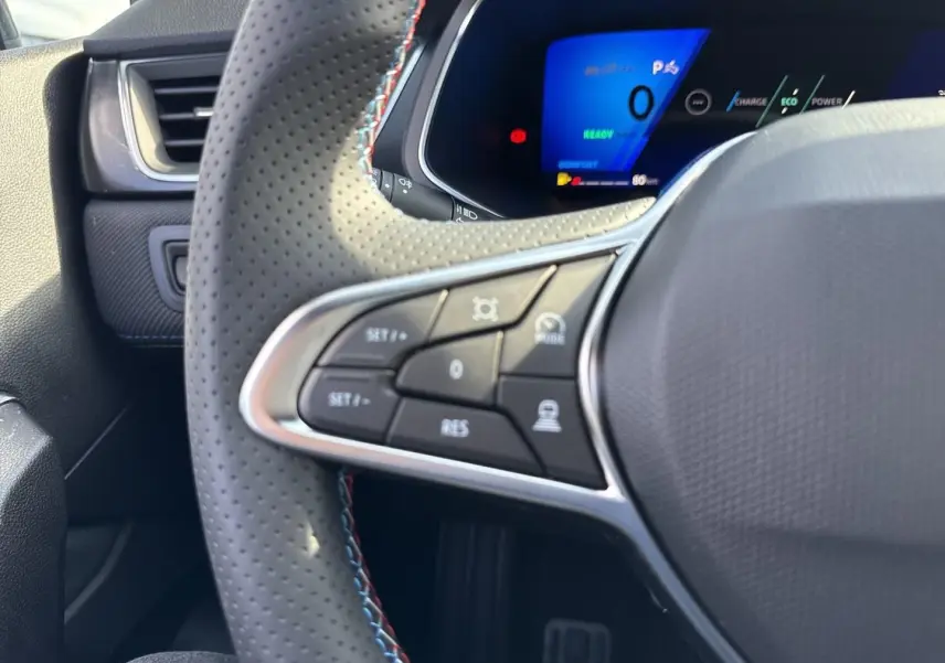 Gros plan sur le volant perforé côté gauche du Renault Symbioz blanc nacré avec commandes multifonctions et tableau de bord digital.