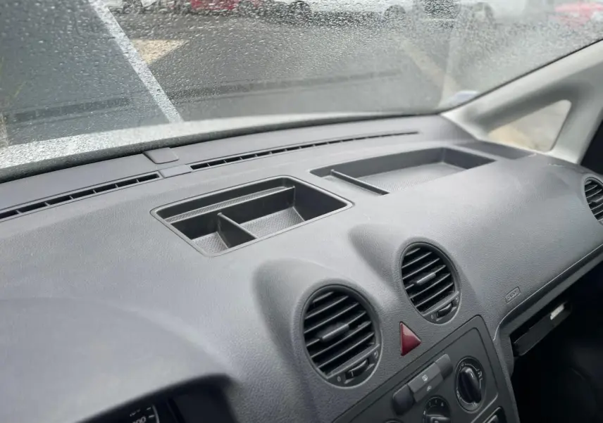 Tableau de bord noir du Volkswagen Caddy 2014 vu de l'intérieur côté passager, avec aérateurs ronds et rangement intégré.