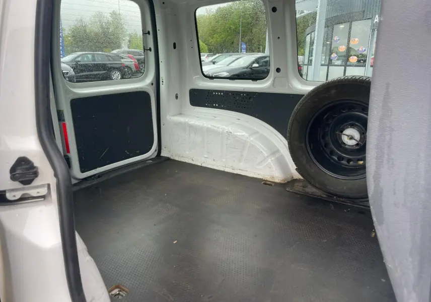 Intérieur du coffre du Volkswagen Caddy blanc Candy 2014, vue arrière droite avec roue de secours visible.