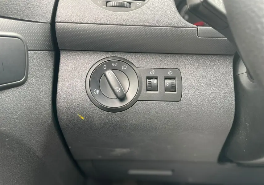 Gros plan sur le bouton de réglage des phares dans l'habitacle du Volkswagen Caddy blanc Candy de 2014.