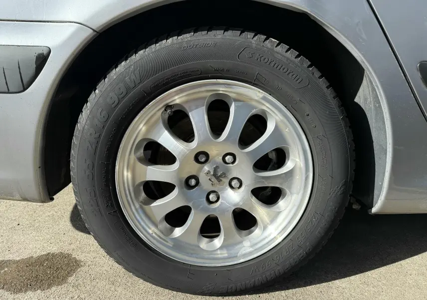 Gros plan sur la roue avant gauche grise d'une Peugeot 607 2.2 i 160 Executive avec jante alu à dix branches.