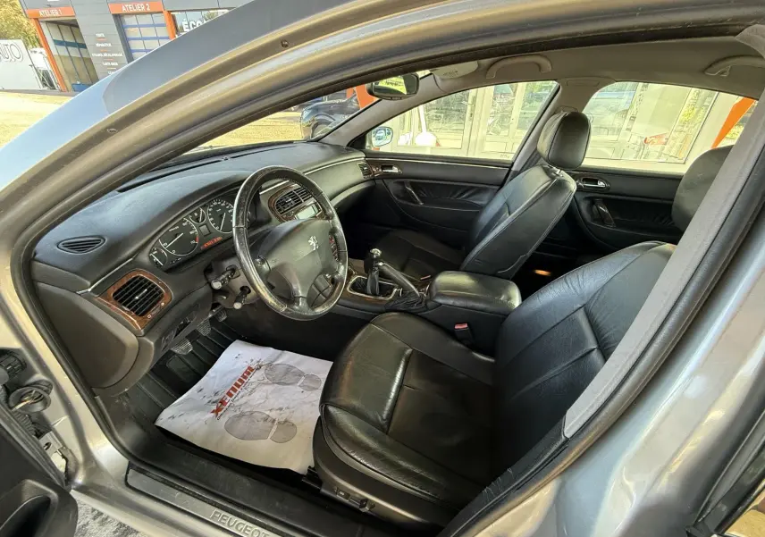 Intérieur d'une Peugeot 607 gris, vue côté conducteur, sièges cuir noir et tableau de bord avec bois.