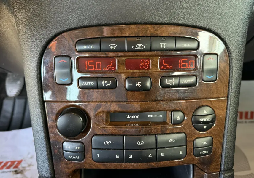 Tableau de bord en bois foncé de Peugeot 607 gris, avec commandes climatisation et autoradio Clarion visibles.