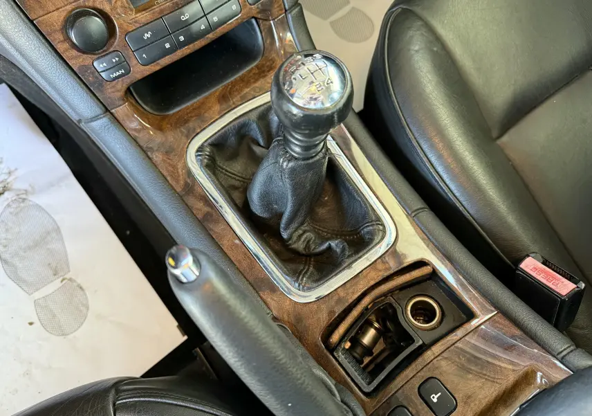 Gros plan sur la console centrale en bois avec levier de vitesse manuel et siège cuir noir d'une Peugeot 607 gris.