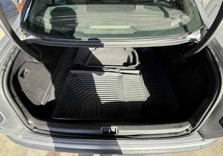 Coffre ouvert d'une Peugeot 607 grise, vue plongeante montrant tapis de sol en caoutchouc et moquette.