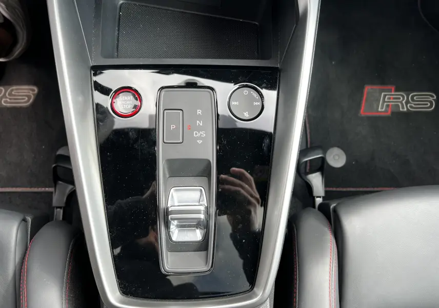 Vue rapprochée de la console centrale noire brillante de l'Audi RS3 Sportback 2022 avec bouton start rouge et tapis RS noir.