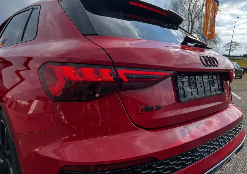 Vue 3/4 arrière droite d'une Audi RS3 Sportback rouge avec feux LED et logo RS3 visible sur le hayon.