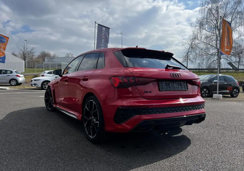 Audi RS3 Sportback rouge vue 3/4 arrière droit, avec jantes noires et double sortie d'échappement sportive.